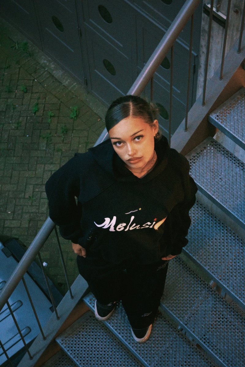 A Famista in the Outta Sight hoodie on a metal fire stair, looking up at the camera